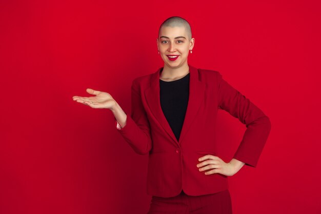 Mostrando, presentando. Retrato de joven mujer calva caucásica aislada en la pared roja.