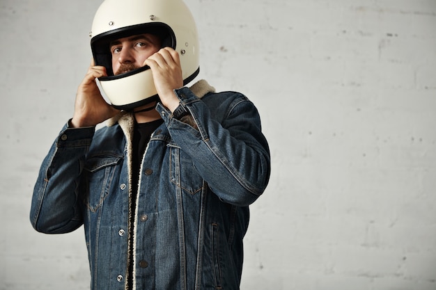 Motociclista caucásico lleva su casco en la cabeza, vistiendo chaqueta vaquera de piel de oveja