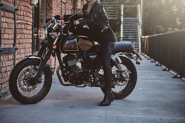 Una motociclista con estilo está sentada en su bicicleta negra mientras posa para una sesión de fotos en la calle.