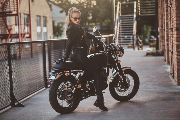 Una motociclista con estilo está sentada en su bicicleta negra mientras posa para una sesión de fotos en la calle.