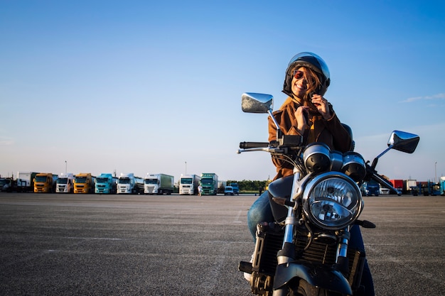 Motociclista mujer sexy sentada en una motocicleta de estilo retro y abrocharse el cinturón del casco antes de viajar