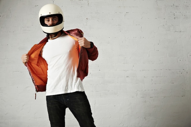 Motociclista serio mostrando el forro naranja de su chaqueta de aire burdeos con casco vintage aislado en blanco