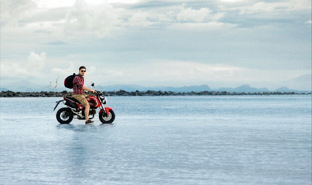 Motorista posando con su motocicleta en el agua de mar