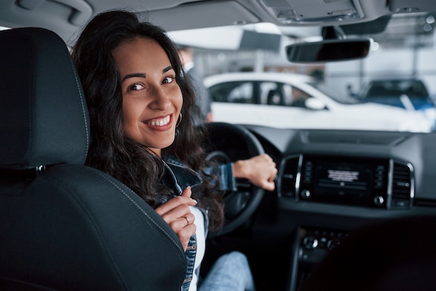 Moviéndose hacia atrás. ute chica con cabello negro probando su nuevo y caro coche en el salón del automóvil