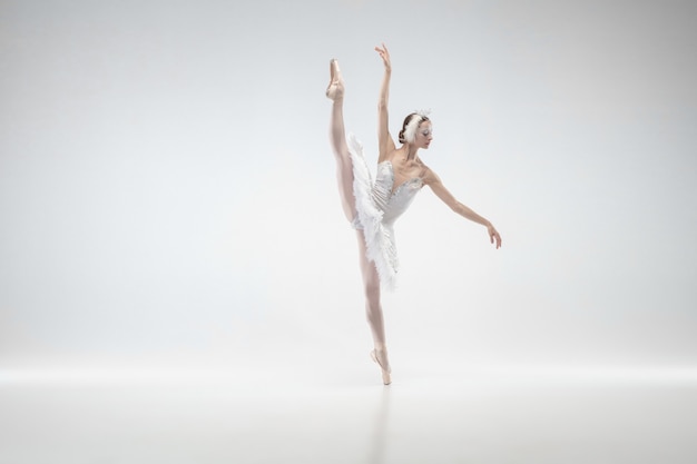 Moviente. Joven bailarina clásica elegante bailando sobre fondo blanco de estudio. Mujer con ropa tierna como un cisne blanco. El concepto de gracia, artista, movimiento, acción y movimiento. Parece ingrávido.