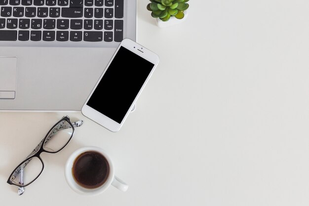 Móvil en la computadora portátil con el espectáculo y la taza de café sobre el escritorio blanco