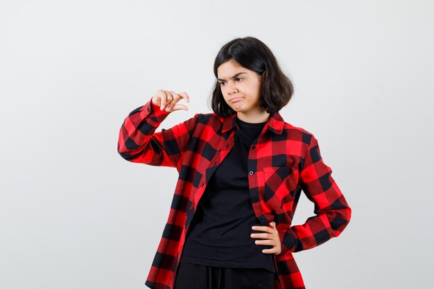 Muchacha adolescente en camiseta, camisa a cuadros que muestra un cartel de tamaño pequeño y que parece insatisfecho, vista frontal.