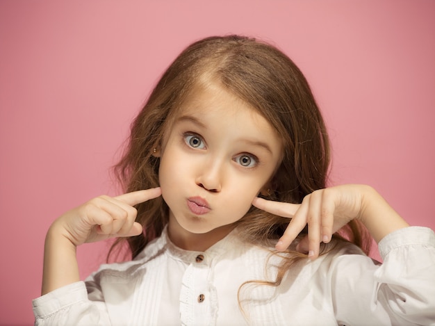 Muchacha adolescente divertida feliz aislada en el fondo rosado moderno del estudio. Hermoso retrato femenino. Niña niña. Las emociones humanas, el concepto de expresión facial. Vista frontal.