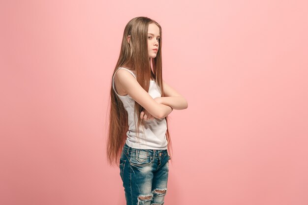 Muchacha adolescente enojada que se coloca en estudio rosado de moda.