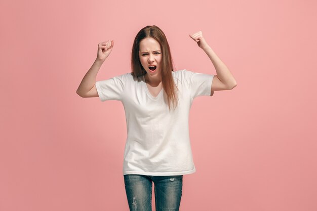 Muchacha adolescente enojada que se coloca en la pared azul de moda. Retrato femenino de medio cuerpo. Las emociones humanas, el concepto de expresión facial. Vista frontal.