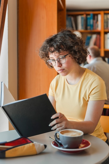 Muchacha adolescente leyendo cerca de café