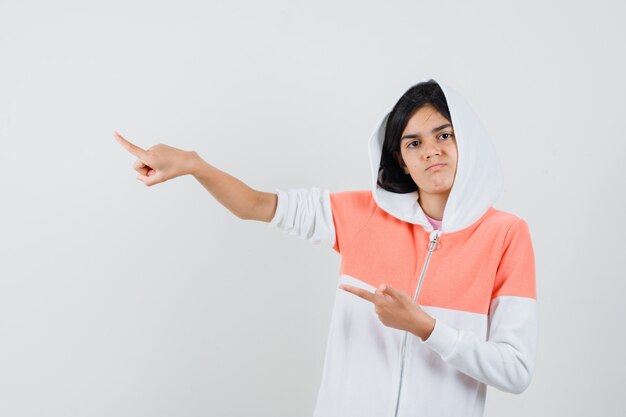 Muchacha adolescente que señala a un lado en la chaqueta blanca y que parece disgustado.