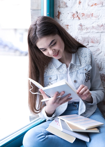 Muchacha del adolescente que se sienta con el libro abierto y que sonríe mientras que lo lee