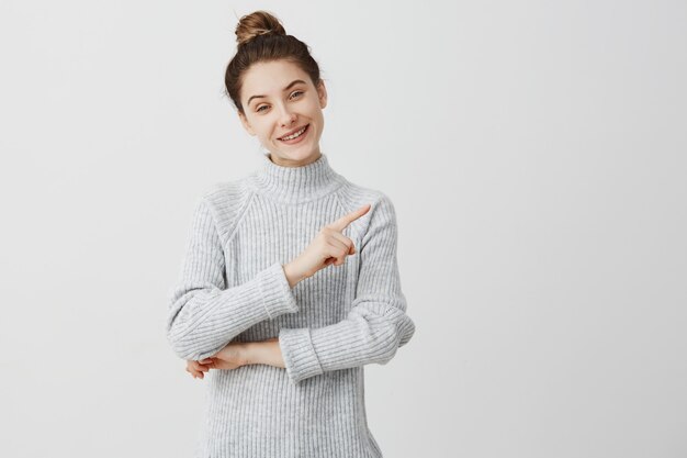 Muchacha adulta hermosa que sonríe mostrando el dedo al lado. Entusiasta femenina presentando su preferencia con el gesto del dedo. Felicidad y disfrute del concepto