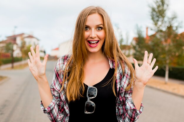 Muchacha alegre bastante rubia joven con la cara de las muecas que mira, posando en campo en día de primavera soleado cálido. Cara graciosa emocional.