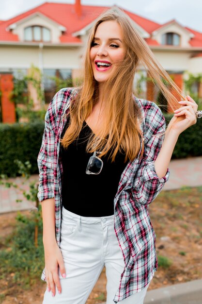 Muchacha alegre bastante rubia joven con la cara sorprendida que mira, posando en campo en día de primavera soleado cálido. Cara graciosa emocional.