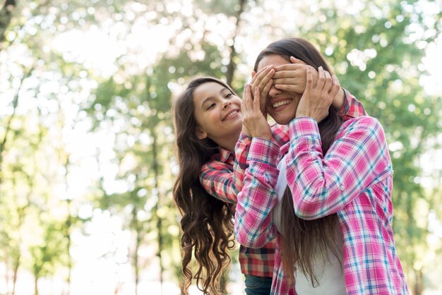 Muchacha alegre que cubre sus ojos de las madres con las manos