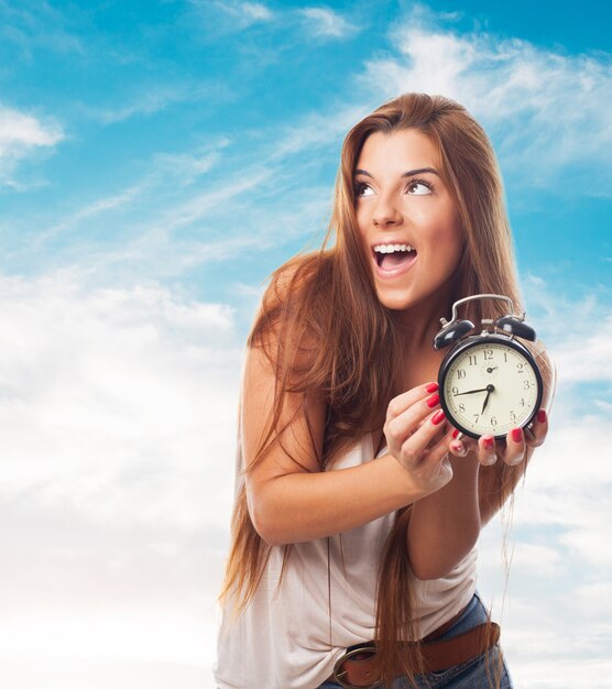 La muchacha alegre con el reloj de alarma