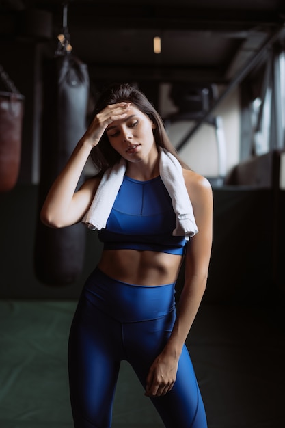 Muchacha apta sonriente que sostiene la toalla y que descansa en gimnasio.