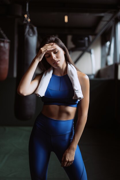 Muchacha apta sonriente que sostiene la toalla y que descansa en gimnasio.