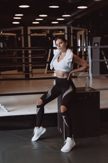 Muchacha apta sonriente que sostiene la toalla y que descansa en gimnasio.