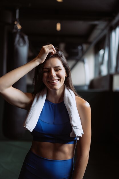 Muchacha apta sonriente que sostiene la toalla y que descansa en gimnasio.