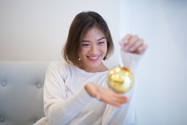 Muchacha asiática emocionada sonriente que sostiene la bola de la Navidad