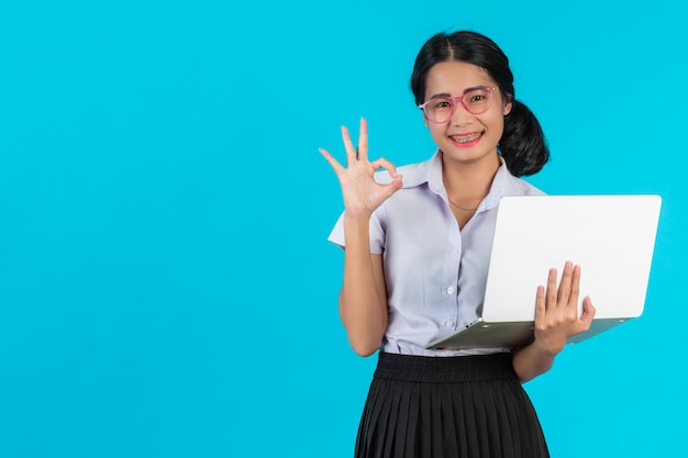 Una muchacha asiática del estudiante que sostiene su cuaderno en un azul.