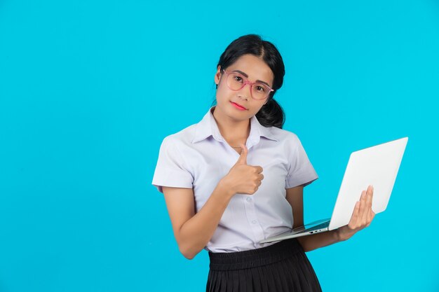 Una muchacha asiática del estudiante que sostiene su cuaderno en un azul.