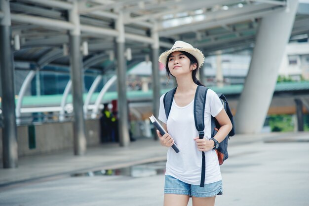 Muchacha asiática sonriente feliz del estudiante con la mochila en el fondo de la ciudad