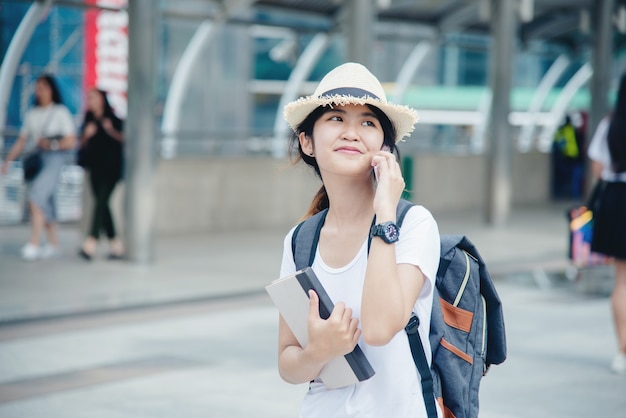 Muchacha asiática sonriente feliz del estudiante con la mochila en el fondo de la ciudad