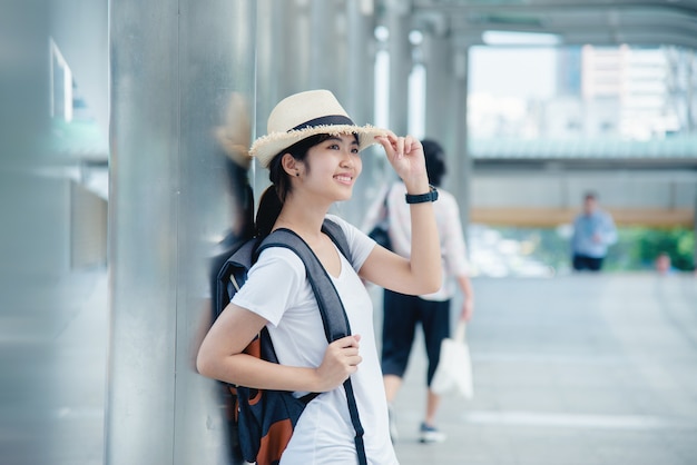 Muchacha asiática sonriente feliz del estudiante con la mochila en el fondo de la ciudad