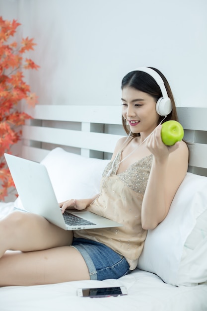 Muchacha con los auriculares que escuchan la música en una computadora portátil en la cama en casa