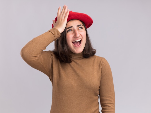 La muchacha bastante caucásica joven molesta con el sombrero de la boina pone la mano en la frente y mira hacia arriba