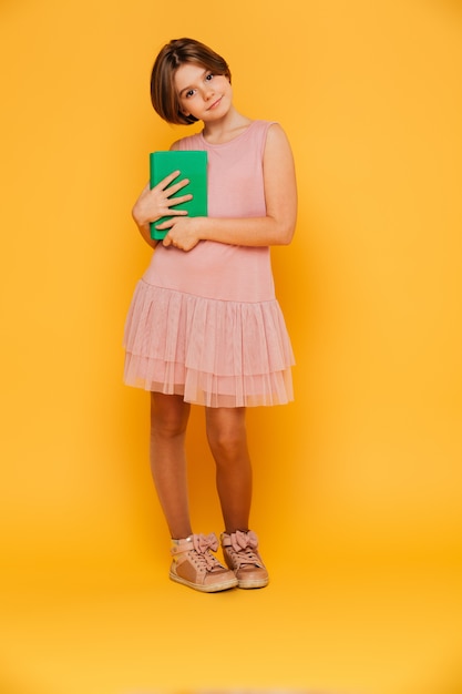 Foto gratuita muchacha bastante pensativa que mira la cámara y que sostiene el libro verde aislado