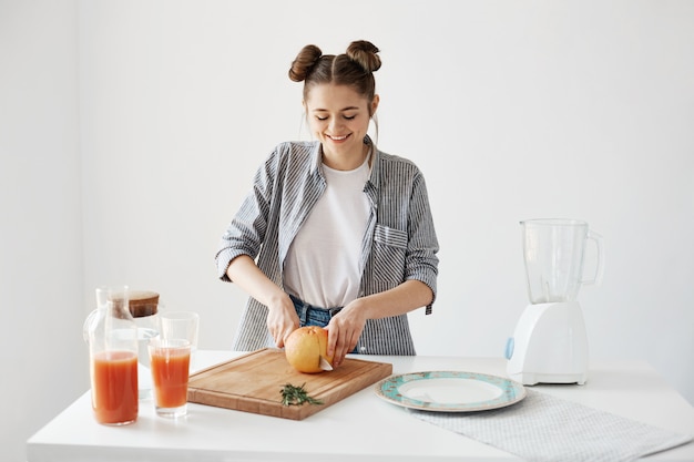 Foto gratuita muchacha bonita alegre que sonríe cortando el pomelo para el desayuno sobre la pared blanca. batido de desintoxicación saludable. comida de fitness.