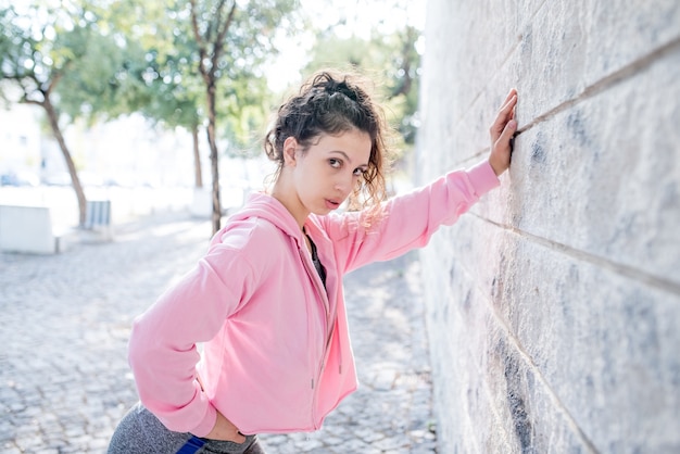 Muchacha bonita deportiva cansada que se inclina en la pared