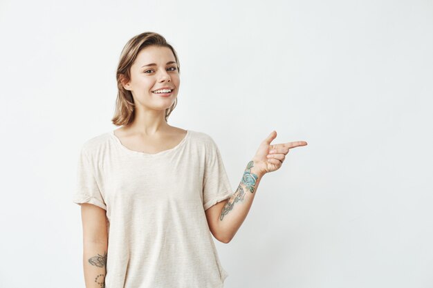 Muchacha bonita joven alegre que sonríe señalando el dedo en lado.