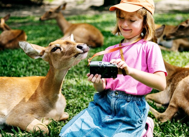 Muchacha caucásica joven que toma el selfie con los ciervos en el parque zoológico