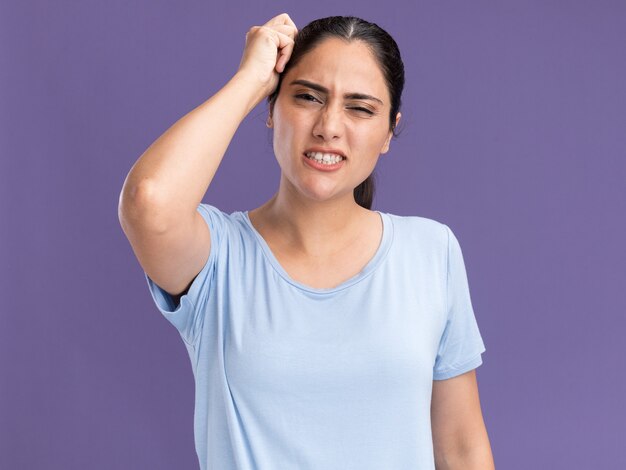 La muchacha caucásica morena joven descontenta pone la mano en la cabeza aislada en la pared púrpura con el espacio de la copia