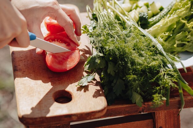 La muchacha corta verduras en el tablero y prepara una ensalada en la naturaleza. día soleado y cocina. Vista de primer plano.