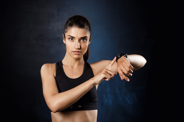 Muchacha deportiva hermosa joven que señala en el vigilar la pared oscura.