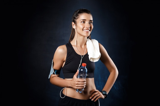 Muchacha deportiva hermosa joven que sostiene el agua sobre la pared oscura.