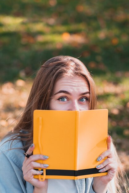 Muchacha divertida que oculta su cara debajo de un cuaderno