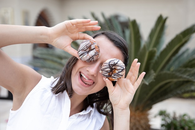 Muchacha divertida que presenta con los buñuelos en el verano afuera. Concepto de vacaciones y vacaciones.