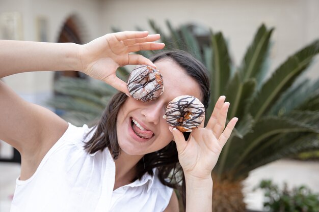 Muchacha divertida que presenta con los buñuelos en el verano afuera. Concepto de vacaciones y vacaciones.