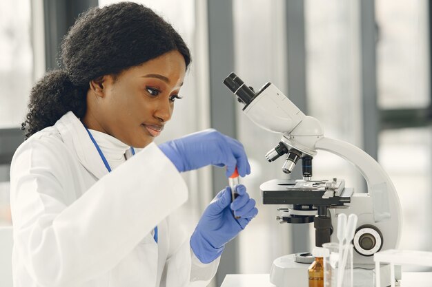 Muchacha del doctor en medicina que trabaja con un microscopio. Joven científica haciendo investigación de vacunas.