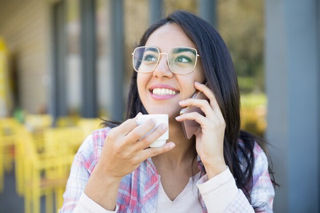 Muchacha elegante positiva del estudiante que disfruta de charla agradable del teléfono