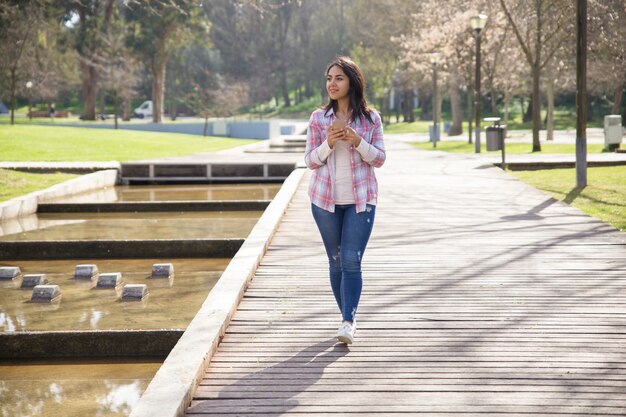 Muchacha encantada sonriente que disfruta de paisaje en parque de la ciudad