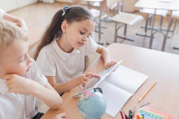 Muchacha de la escuela con tableta cerca de niño